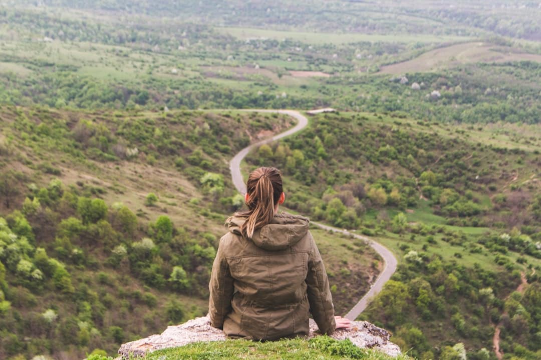 Photo by Vlad Bagacian woman sitting on grey cliff